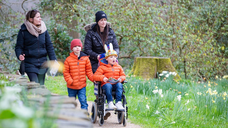 Two women walking in a garden with two children, one of the children is in a wheelchair